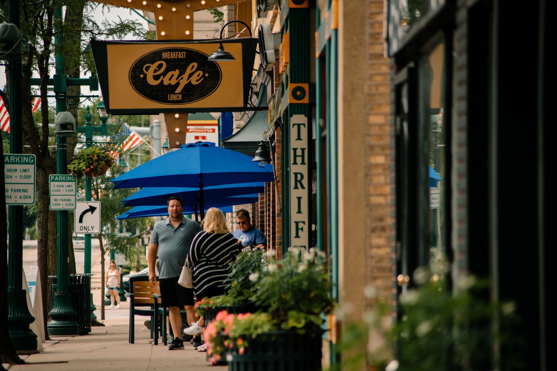 Cafe exterior with blue umbrellas, people walking on the sidewalk, and a