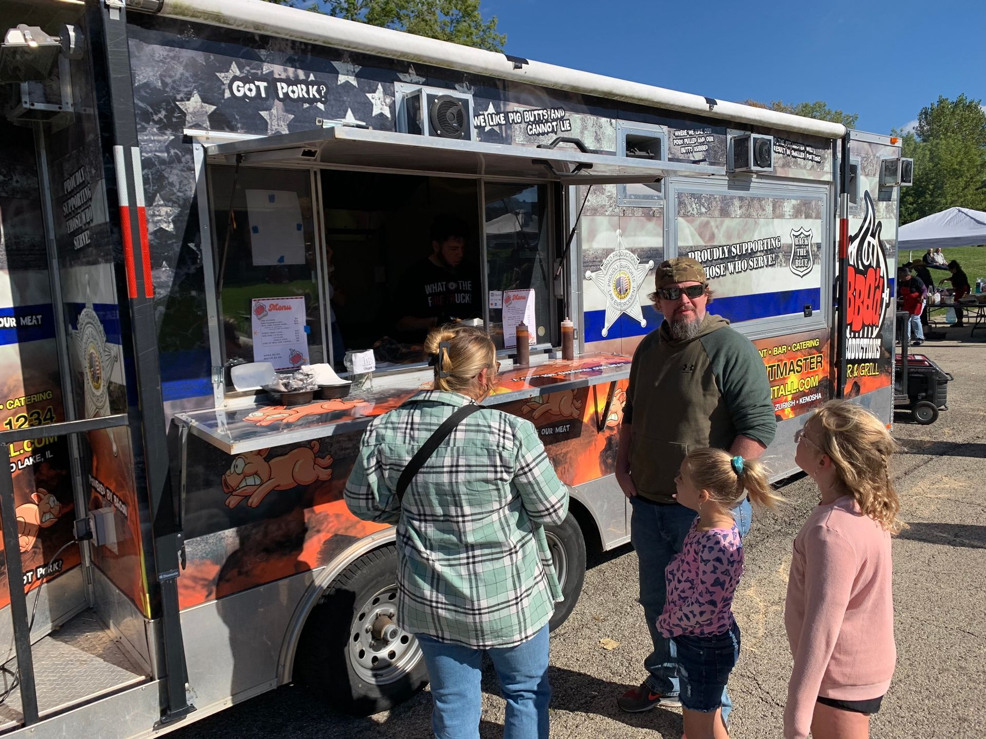 Food truck with customers. People ordering and waiting for food. Outdoors, sunny.