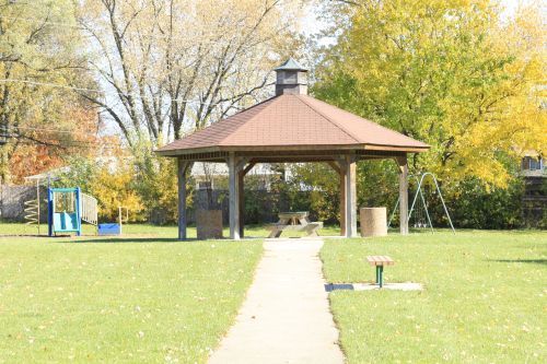 Gazebo in a park with a pathway, playground equipment, and trees.