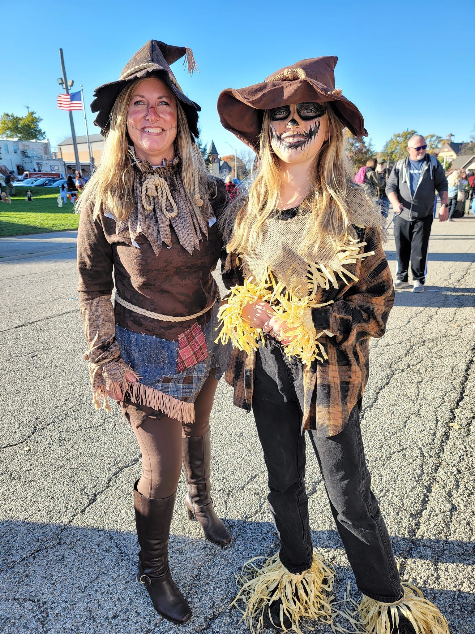 Two women in scarecrow costumes, posing outdoors on a sunny day.