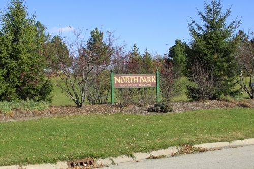Sign for North Park in a grassy area, with trees and a blue sky.