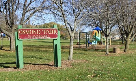 Osmond Park sign in a green grassy area with a playground in the background.