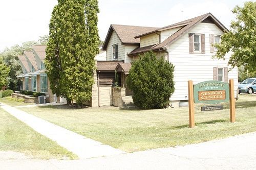 Exterior view of the senior center, a two-story light-colored building with a sign on the lawn.
