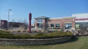 A brick building with a dark blue sign. A red pole stands in a small landscaped island.