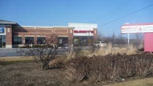 A commercial building with a red sign, clear sky, and dry bushes.