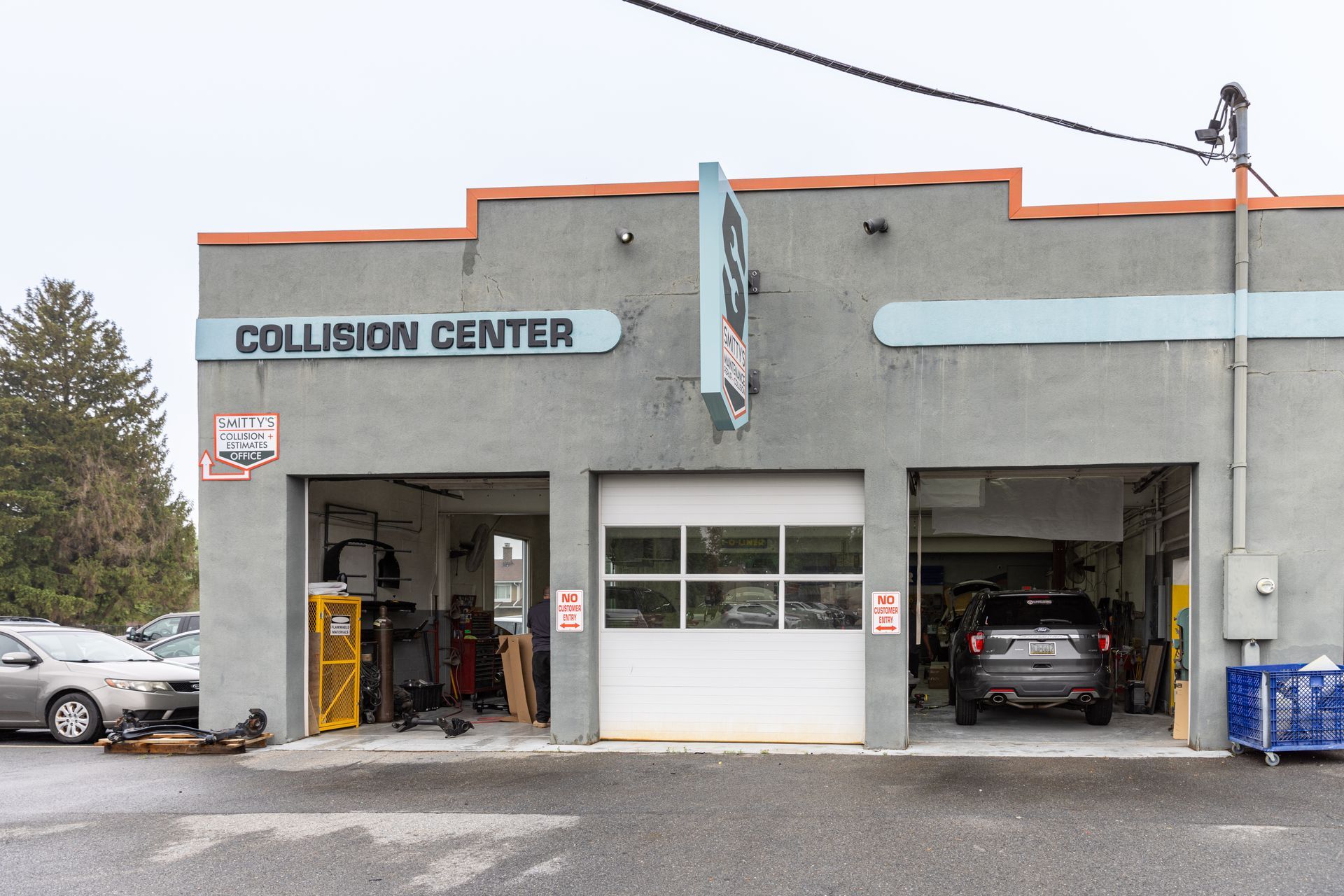 A gray auto collision center with three garage bays and parked cars.