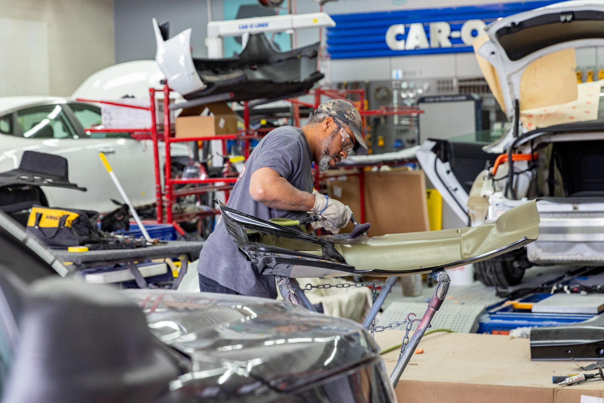 Mechanic working on a car part in an auto body shop. Grey-haired man using tools. Blue and white shop interior.