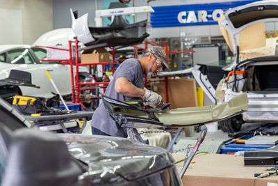 Mechanic working on a car frame in a brightly lit repair shop.