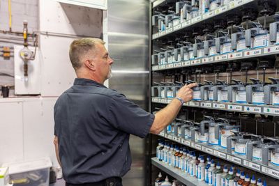 Man in a shop selects paint from a wall-mounted cabinet filled with labeled paint cans.