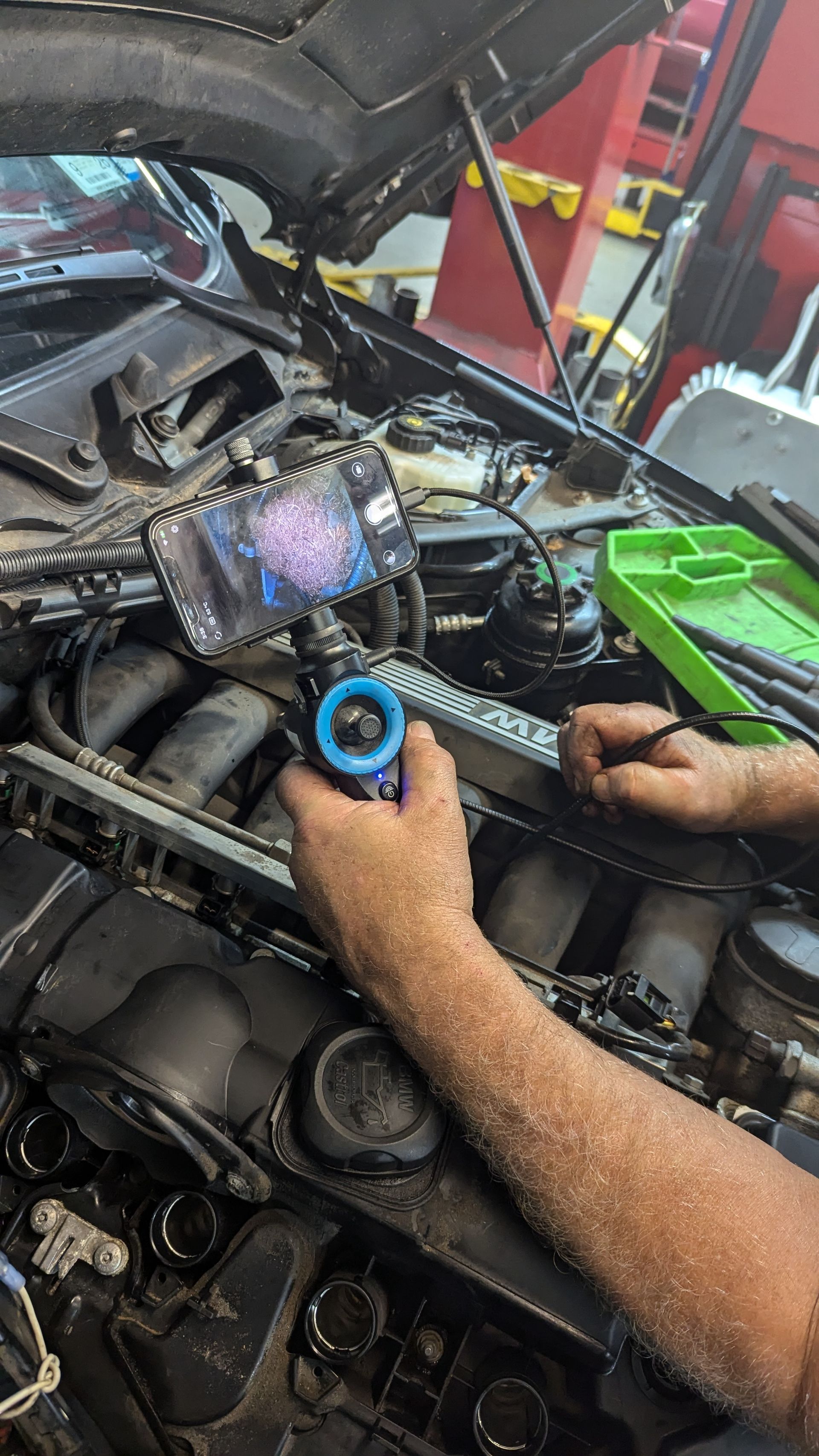Mechanic using a borescope with a phone attachment to inspect an engine compartment.