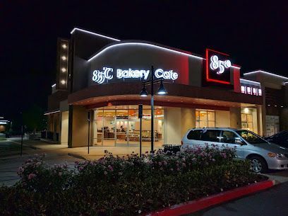 A white van is parked in front of a bakery cafe at night.