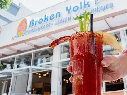 tree service close to me-Bloody Mary with garnish at Broken Yolk Cafe. Hand holding glass, restaurant in background.