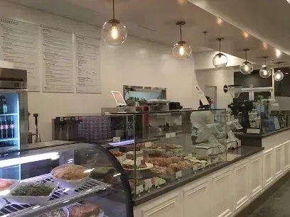 tree service close to me-A cafe interior with glass display cases filled with baked goods, menu boards on the wall, and globe pendant lights.