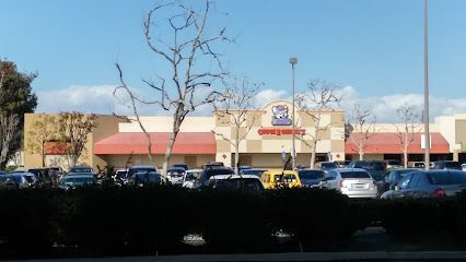 Tree service close to me-Baseball field, green and brown turf, backstop with signage, tall light poles, overcast sky.