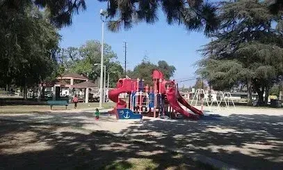 tree service close to me-Playground in a park with red slides, benches, and trees.