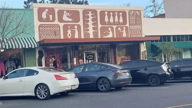 tree service close to me-Storefront with brown mural depicting figures; cars parked in front.