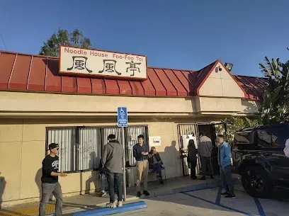 A group of people are standing outside of a restaurant called noodle house