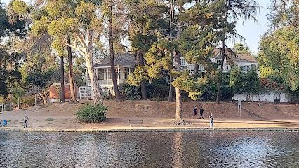 Lake view with a white house, trees, and people walking by the water.