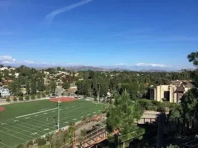 tree service close to me-Football field and baseball field viewed from above, surrounded by trees, buildings, and a mountain range under a blue sky.