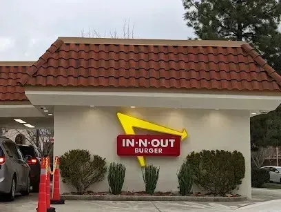 tree service close to me-In-N-Out Burger restaurant with cars in drive-thru lane. Yellow logo on red sign, beige building, brown roof.