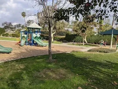 Tree service close to me-Playground in a park with slides, swings, and grassy areas under a cloudy sky.