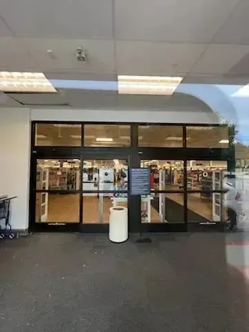tree service close to me-Exterior view of store entrance with automatic doors, trash can, and shopping cart.