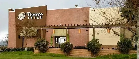 tree service close to me- Bread restaurant exterior with brown and beige walls, sign, and landscaping.