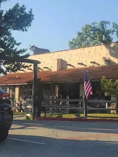 tree service close to me-Restaurant with brown roof, wooden fence, and American flag; a cow sculpture on the roof.