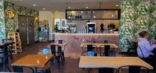 tree service close to me-Interior of a cafe with tables, a bar, and floral wallpaper. A person sits at a table near a window.