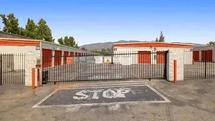 tree service close to me-Storage units behind a gated entrance, painted white and orange, with mountains in the background under a blue sky.