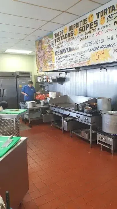 tree service close to me-Restaurant kitchen with stainless steel equipment and a cook preparing food. Red tile floor, menu board.