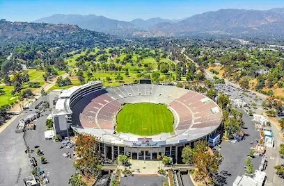 An aerial view of a large stadium surrounded by trees and mountains.