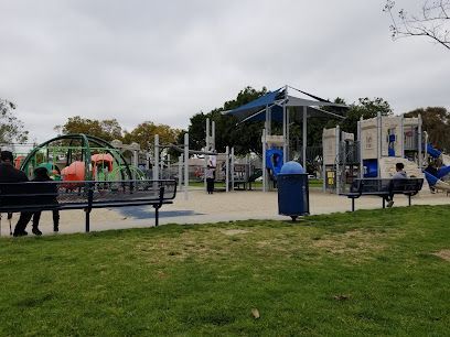 Tree service close to me-Playground with green and yellow structures, a carousel, and wood chip ground under a blue sky.