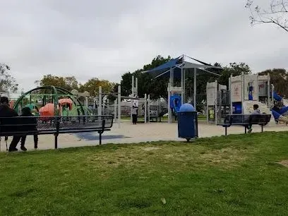 Tree service close to me-Playground with green and yellow structures, a carousel, and wood chip ground under a blue sky.