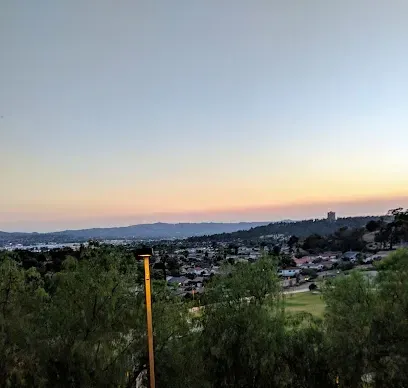 A sunset over a city with trees in the foreground and mountains in the background.