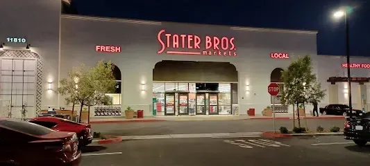 A stater bros store is lit up at night with cars parked in front of it.