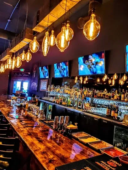 A long wooden bar in a restaurant with lots of lights hanging from the ceiling