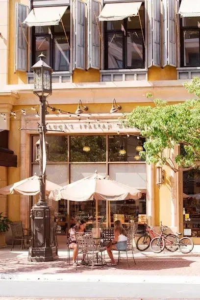 tree service close to me- exterior with outdoor seating, umbrellas, and bikes. Building has tan facade, shuttered windows. People seated at tables.