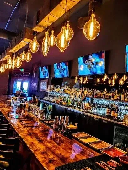 tree service close to me-Bar interior with a wooden bar, hanging lights, televisions, and bottles.