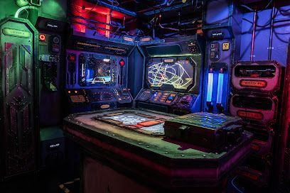 Dark, futuristic control room with glowing screens, wires, and a central table. Neon red, blue, and green lighting.