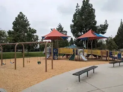 tree service close to me-Playground with swings, slides, and shade structures; overcast sky.