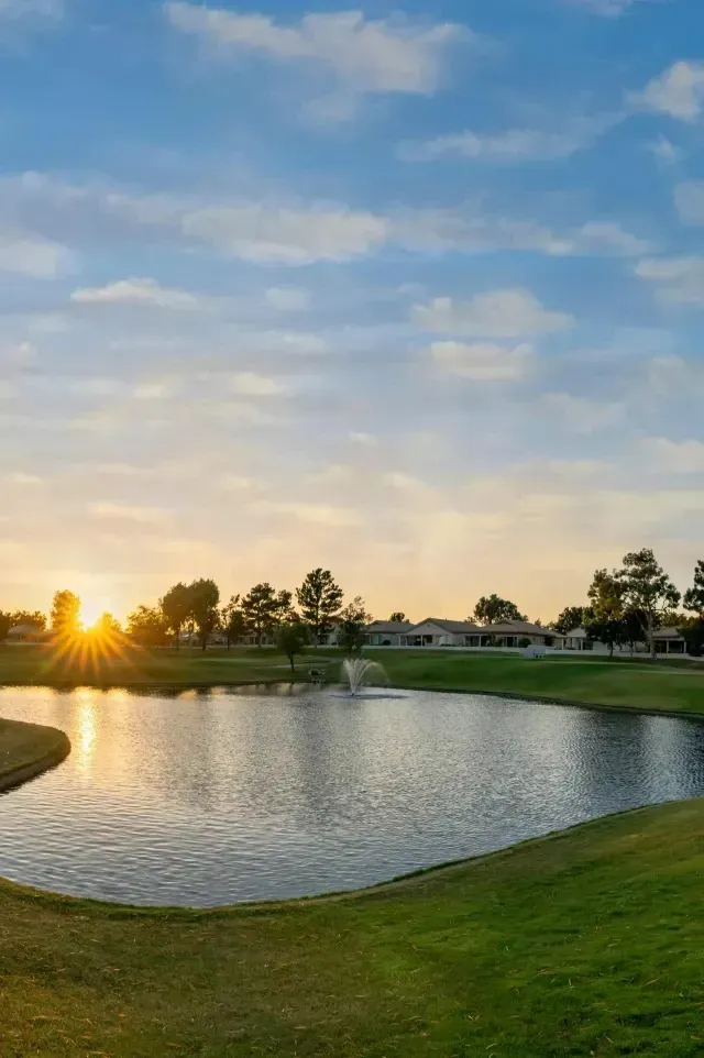 Tree Service Close to me-Pond on a golf course at sunrise, with bright yellow sun and blue sky.