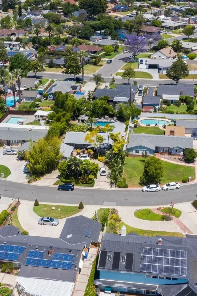 Tree Service-Aerial view of a suburban neighborhood with houses, trees, and roads. Some houses have solar panels on their roofs.
