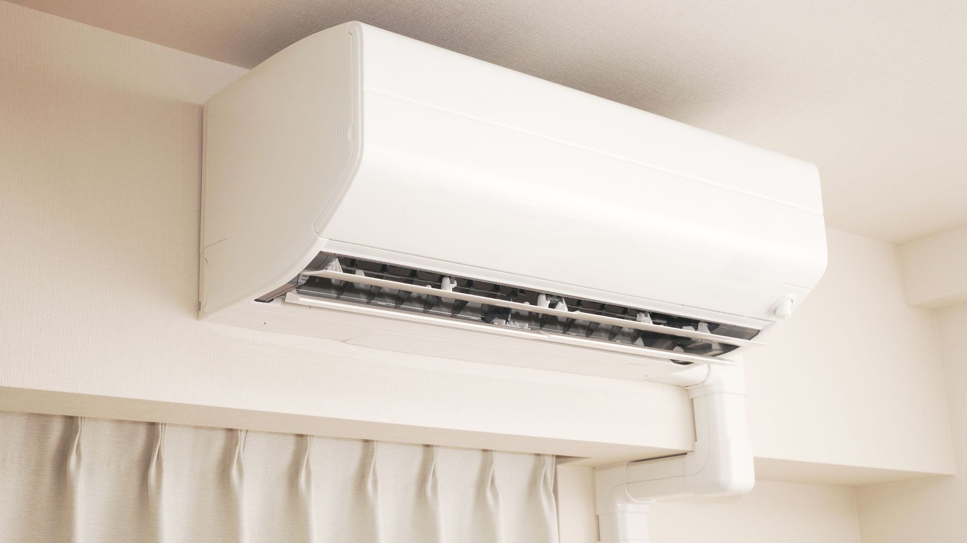 A white air conditioner is hanging from the ceiling in a room next to a window.