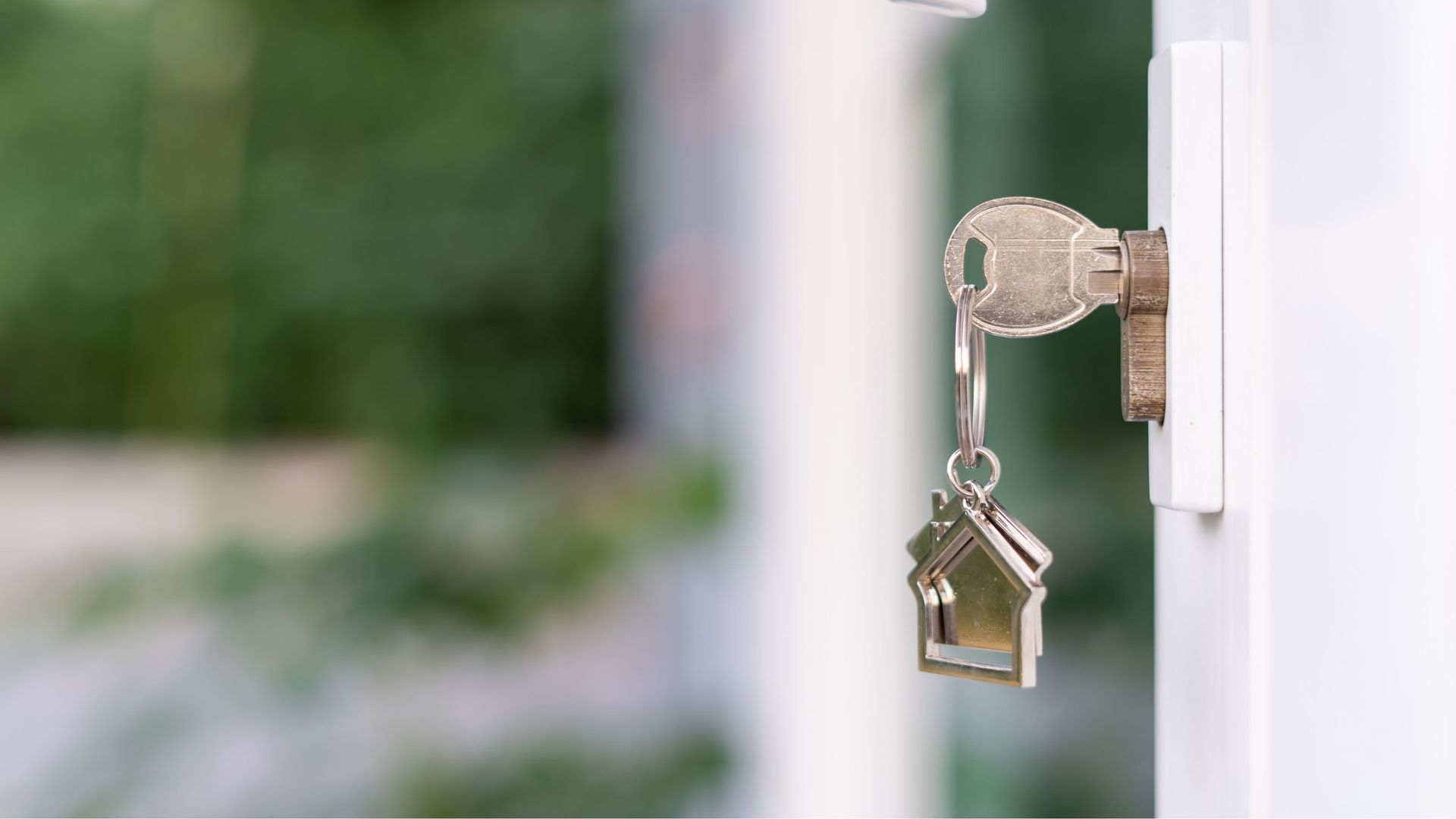 A close up of a key in a door lock with a keychain in the shape of a house.