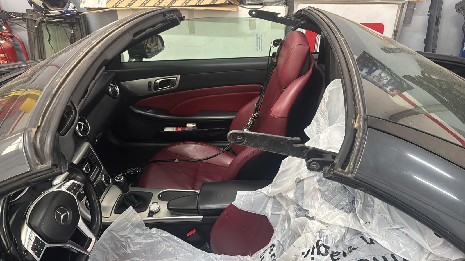 Vista dell'interno di una Mercedes decappottabile grigia con sedili rossi, pellicola di plastica e capote aperta.