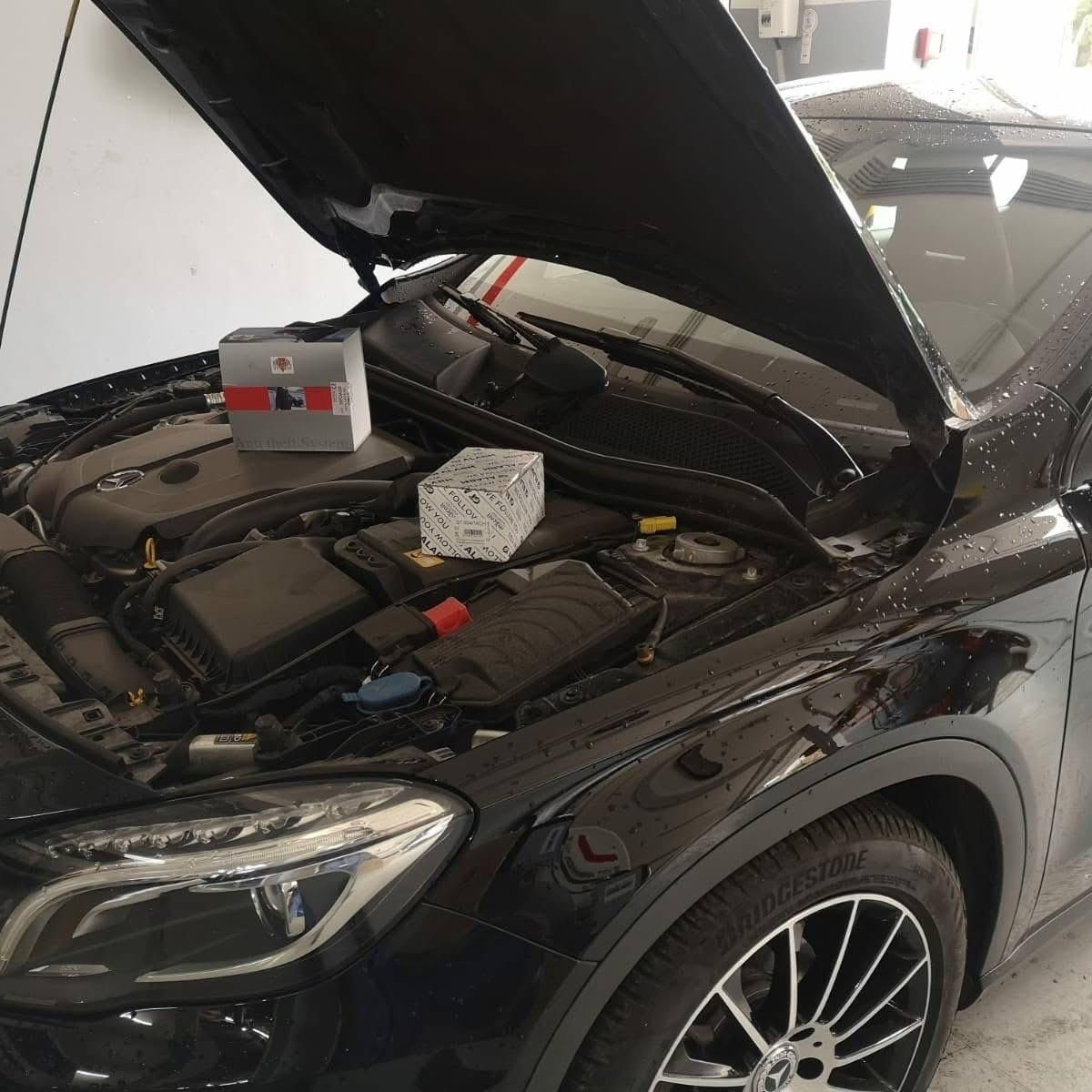 Un'auto nera con il cofano aperto, una batteria e un blocco sul motore in un'officina.