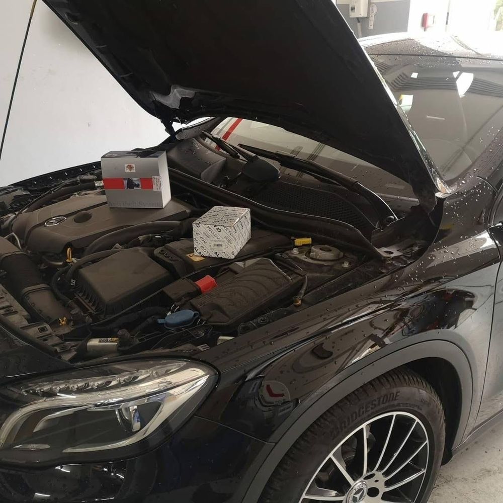 Un'auto nera con il cofano aperto, una batteria e un blocco sul motore in un'officina.