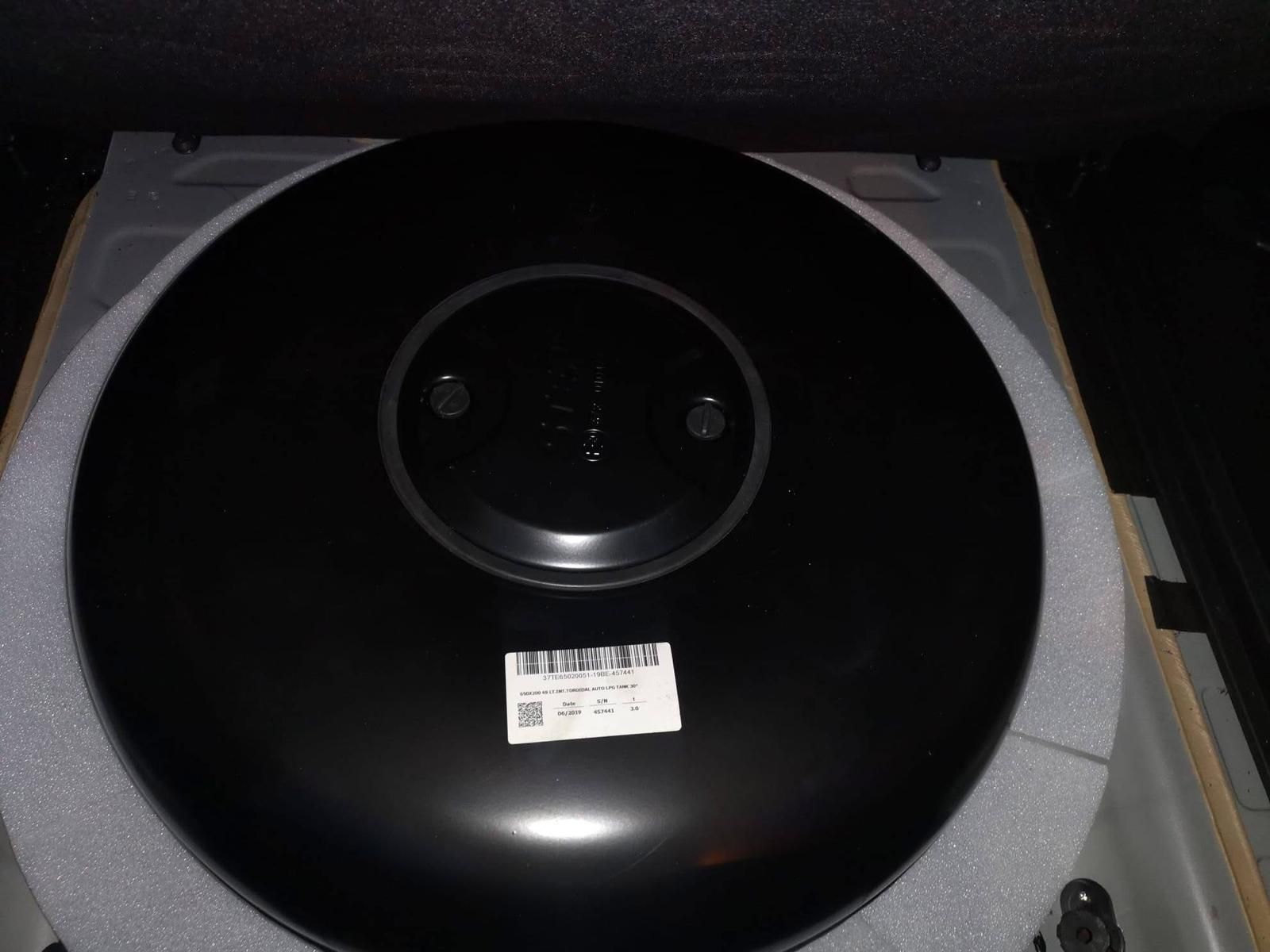 Ruota di scorta nera all'interno del bagagliaio di un'auto, circondata da schiuma bianca. Un'etichetta bianca è attaccata alla ruota.