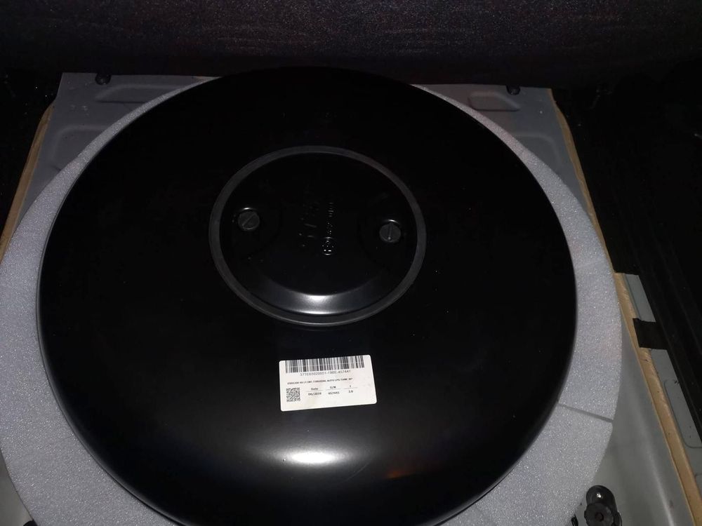 Ruota di scorta nera all'interno del bagagliaio di un'auto, circondata da schiuma bianca. Un'etichetta bianca è attaccata alla ruota.